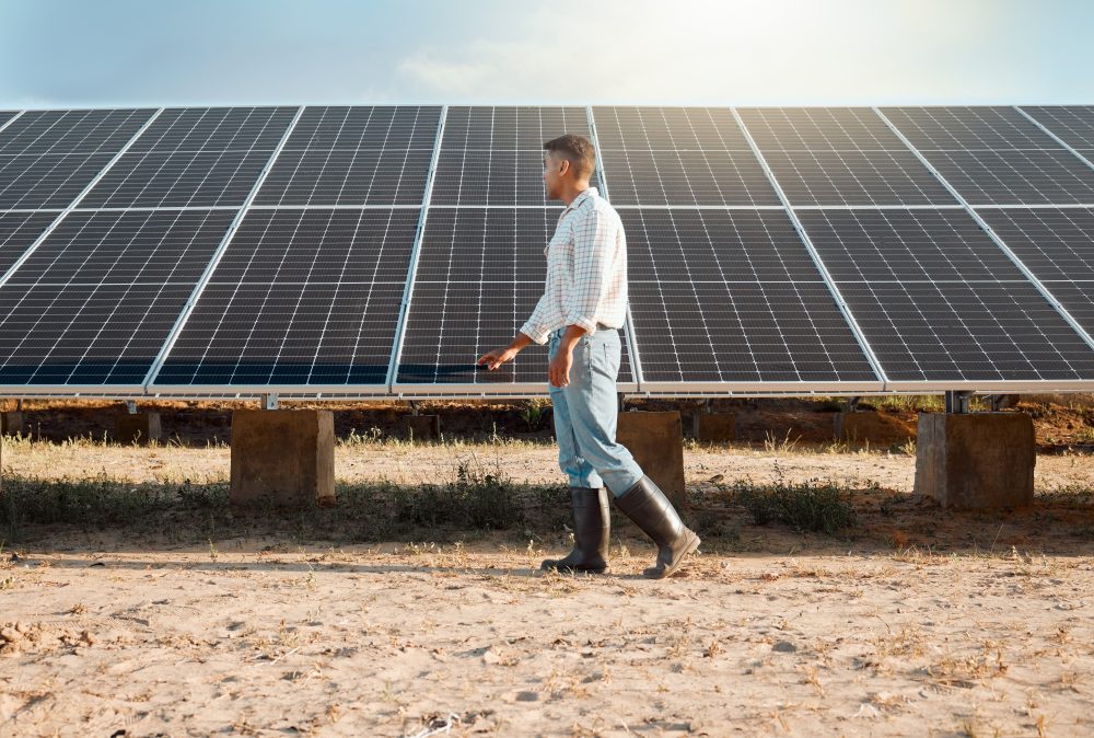 Shot of a young man standing next to a solar panel on a farm.